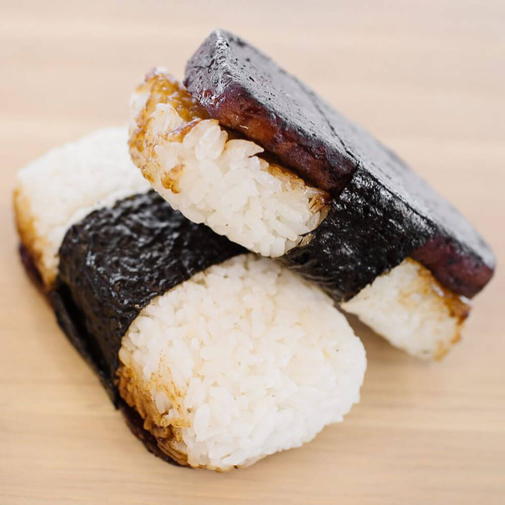 Spam Musubi up close includes combo of rice, seared spam glazed in teriyaki sauce wrapped in dried seaweed.